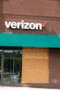 A Verizon store in an outdoor strip mall with a plywood panel covering a broken glass front window