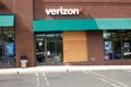 A Verizon store in an outdoor strip mall with a plywood panel covering a broken glass front window