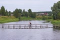 A man on a bicycle crosses a wooden suspension bridge over the river in Verkhovye