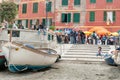 Piazza Marconi crowded with tourists between tatty old building facade and ramp to beach and boats