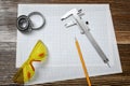 A vernier scale, a pencil, yellow protective glasses and two bearings lying on drafting paper on wooden background.