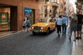 A yellow retro car Saab rides through a crowd of tourists along the narrow street of Verona