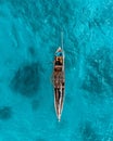 Vertical aerial view of a man sealing his boat on teal ocean waves