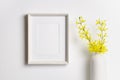 Vertical artwork frame mockup on white wall with yellow plant decor in vase