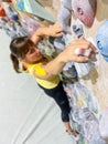 VERTICAL: Athletic female with taped fingers climbs up colorful bouldering wall. Royalty Free Stock Photo