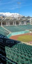 Vertical Baseball field with green tiered seating against mountain and vibrant blue sky