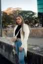 Vertical of a beautiful Argentinian woman in a white coat and blue jeans outdoors