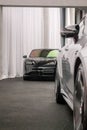 Vertical Porsche Taycan turbos behind grey Mercedes in showroom, black pavement white background