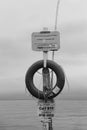 Vertical black and white shot of a buoy with a rope and signs in cloudy sky background