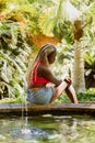 Vertical of a black woman with blonde braids sitting near a small fountain looking down Royalty Free Stock Photo