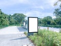 Vertical blank advertising poster banner mockup at empty bus stop shelter by main road, greenery behind; out-of-home OOH vertical Royalty Free Stock Photo