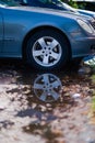 Vertical of a blue Mercedes car wheel reflecting in a puddle of water.