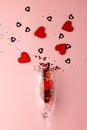 Vertical of champagne glass spilling red heart shapes on pale pink background with copy space