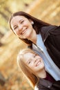 Vertical cheerful, glad, laughing family, mother and little daughter look at camera, stroking and stand in autumn park