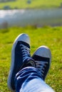 Vertical close-up of a blue and white pair of shoes relaxing on a green meadow with a defocused lake in the background Royalty Free Stock Photo