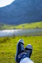 Vertical close-up of a blue and white pair of shoes relaxing on a green meadow with a defocused lake in the background Royalty Free Stock Photo