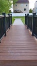 Vertical Close up of bridge with brown wood deck and black guardrail over a grassy pond