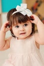 Vertical close up indoor portrait of cute happy baby girl playing with dressy white headband