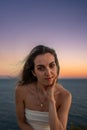 Vertical Close-Up portrait Capture of a Young Woman in a White Dress, with a Gold Necklace, sitting by the Ocean at Sunset, Hair Royalty Free Stock Photo