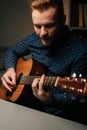 Vertical close-up portrait of guitarist singer male playing acoustic guitar and singing favorite song in dark living