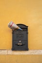 Vertical close-up of a post box stuffed with a newspaper on a bright yellow wall, Florence, Italy