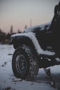 Vertical close-up shot of a Jeep wrangler covered in snow at sunset on a cold winter day