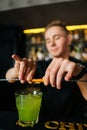 Vertical close-up shot of young barman bartender male squeezing out piece of orange peel with straw and decorating