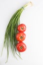 Vertical close up top view shot of a bunch of green onions and three ripe red tomato on a white background Royalty Free Stock Photo