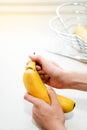 Vertical close up view of banana being open and ripped from the top by young woman above the kitchen counter