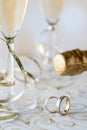 A vertical close up of wedding bands with champagne flutes, gold ribbon and a the top of a champagne bottle in behind. Royalty Free Stock Photo