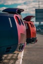 Vertical closeup of back parts of a red and purple racing cars with spoilers blurred sky background