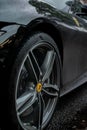 Vertical closeup of a black Ferrari wheel with rain drops in Hale Village, United Kingdom