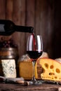 Vertical closeup of a bottle of red wine pouring into a glass with a cheese assortment Royalty Free Stock Photo