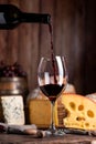 Vertical closeup of a bottle of red wine pouring into a glass with a cheese assortment Royalty Free Stock Photo