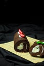 Vertical closeup of chocolate swiss rolls with berries in a straw plate, dark background