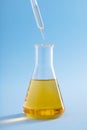 Vertical closeup of a dropper over an Erlenmeyer flask with yellow liquid on a blue background