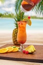 Vertical closeup of a glass of cocktail, a slice of lemon pineapple near, beach blurred background