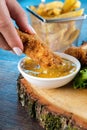 Vertical closeup of a hand dipping chicken nugget in a sauce