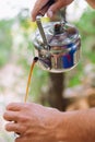 Vertical closeup of hands holding a cup and pouring coffee into it from a metallic kittle