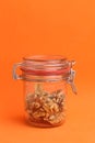 Vertical closeup of a jar of cracked walnuts inside on an orange background Royalty Free Stock Photo