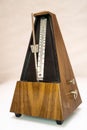 Vertical closeup of an old-style wooden metronome on a white surface.