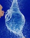 Vertical closeup of a person popping a water balloon with a needle against a blue background Royalty Free Stock Photo