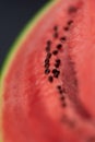A vertical closeup portrait of the black seeds sitting in the pink red pulp of a cut slice of green watermelon. The piece of fruit