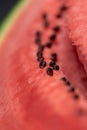 A vertical closeup portrait of the black seeds sitting in the pink red pulp of a cut slice of watermelon. The piece of fruit is