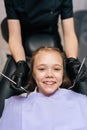 Vertical closeup portrait of happy cute little girl smiling looking at camera sitting in stomatology seat while dentist Royalty Free Stock Photo