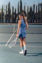 Vertical closeup of a rear female tennis player on a court holding racquet in a hand