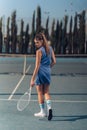 Vertical closeup of a rear female tennis player on a court holding racquet in a hand