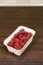 Vertical closeup shot of fresh raspberries in a white plastic bowl on a wooden table Royalty Free Stock Photo