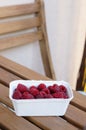 Vertical closeup shot of fresh raspberries in a white plastic bowl on a wooden table Royalty Free Stock Photo