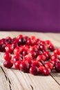 Vertical closeup shot of fresh red cranberries on a wooden table with a purple background Royalty Free Stock Photo